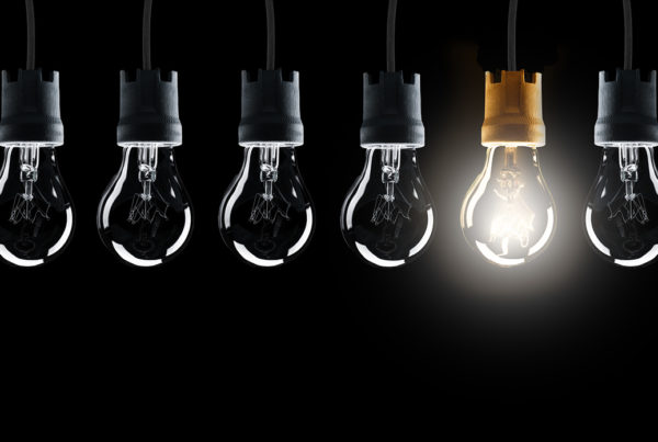 Light bulbs in row with single one shinning, isolated on black