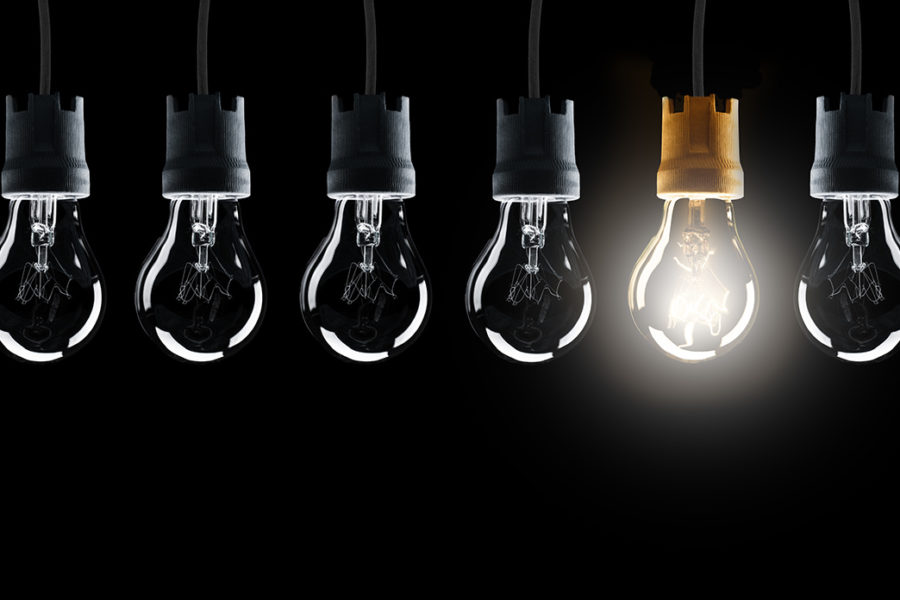 Light bulbs in row with single one shinning, isolated on black